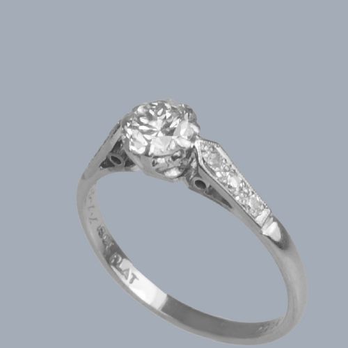 fig 4. An Art Deco diamond solitaire ring featuring a round central diamond flanked by geometric shoulders set with small accent diamonds in white gold and platinum.