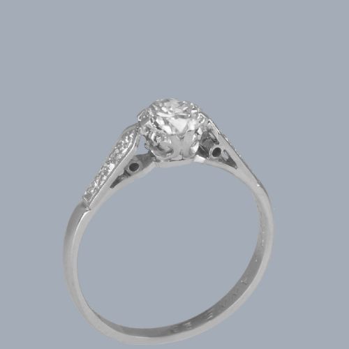 fig 5. An Art Deco diamond solitaire ring featuring a round central diamond flanked by geometric shoulders set with small accent diamonds in white gold and platinum.