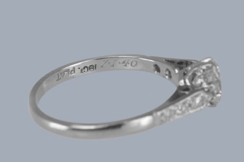 fig 6. An Art Deco diamond solitaire ring featuring a round central diamond flanked by geometric shoulders set with small accent diamonds in white gold and platinum.