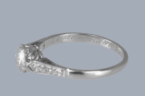 fig 7. An Art Deco diamond solitaire ring featuring a round central diamond flanked by geometric shoulders set with small accent diamonds in white gold and platinum.