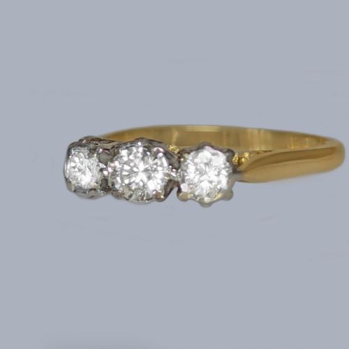 fig 3. A three-stone round diamond trilogy ring set in white metal claw mounts on an 18ct yellow gold band.