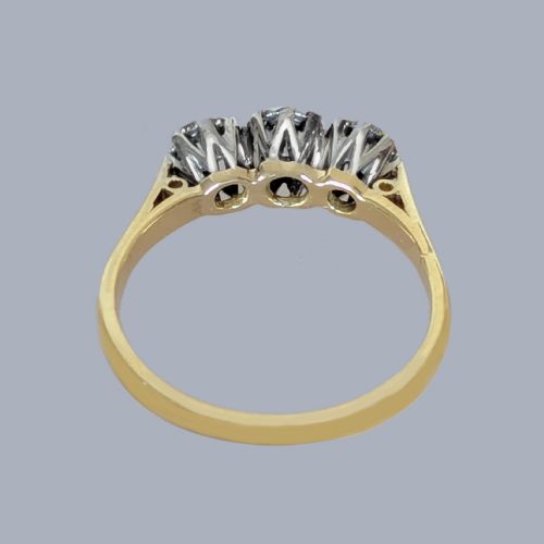 fig 5. A three-stone round diamond trilogy ring set in white metal claw mounts on an 18ct yellow gold band.
