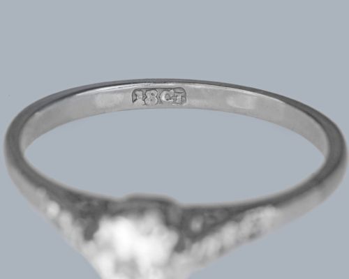 fig 4. An 18ct white gold solitaire ring showcasing a central round diamond in a claw setting flanked by small diamonds in the shoulders.