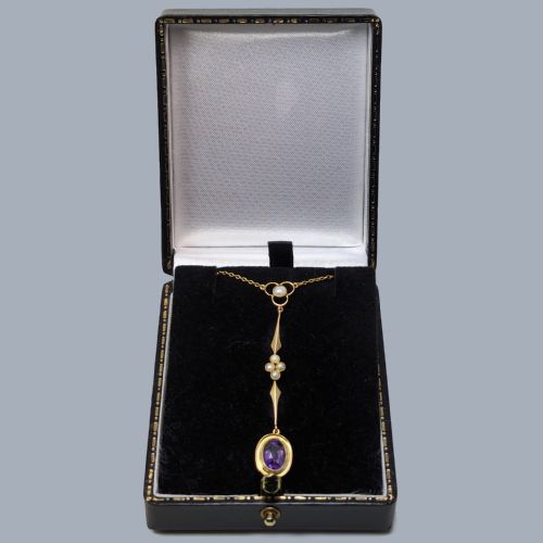 fig 5. An Edwardian 9ct gold drop necklace featuring a fine chain suspending an elongated linear pendant set with seed pearls and an oval-cut amethyst.