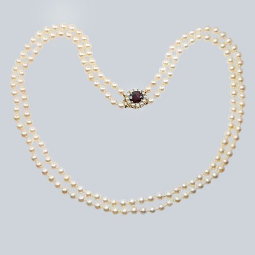 fig 1. A double strand cultured pearl necklace featuring uniform cream pearls fastened with a round 9ct gold clasp inset with a dark red garnet stone.