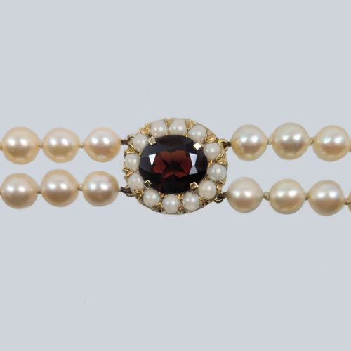 fig 2. A double strand cultured pearl necklace featuring uniform cream pearls fastened with a round 9ct gold clasp inset with a dark red garnet stone.