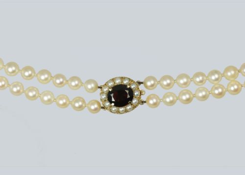 fig 5. A double strand cultured pearl necklace featuring uniform cream pearls fastened with a round 9ct gold clasp inset with a dark red garnet stone.