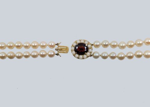 fig 6. A double strand cultured pearl necklace featuring uniform cream pearls fastened with a round 9ct gold clasp inset with a dark red garnet stone.