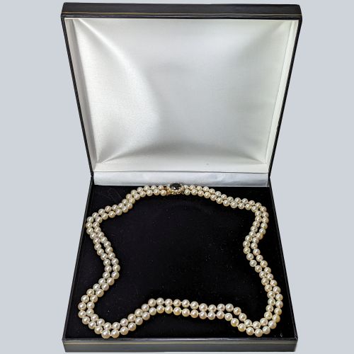 fig 7. A double strand cultured pearl necklace featuring uniform cream pearls fastened with a round 9ct gold clasp inset with a dark red garnet stone.