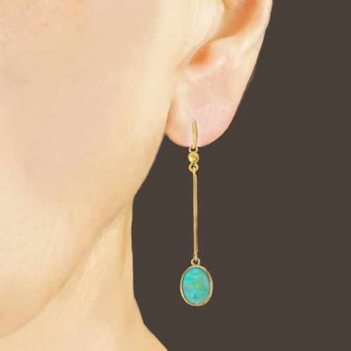 fig 1. A pair of vintage 18 carat yellow gold drop earrings featuring slender vertical bars suspended from wire hooks and terminating in oval opal cabochons displaying blue and green play-of-colour within milgrain settings.
