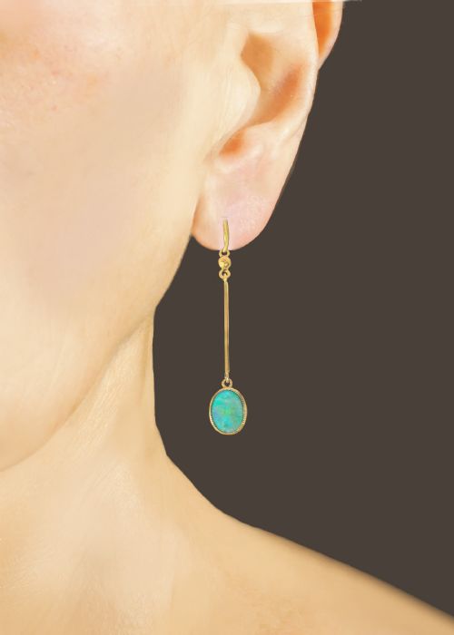 fig 6. A pair of vintage 18 carat yellow gold drop earrings featuring slender vertical bars suspended from wire hooks and terminating in oval opal cabochons displaying blue and green play-of-colour within milgrain settings.