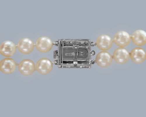 fig 5. A double strand cream pearl necklace featuring a square 18ct white gold clasp set with a central square blue sapphire and accent diamonds.