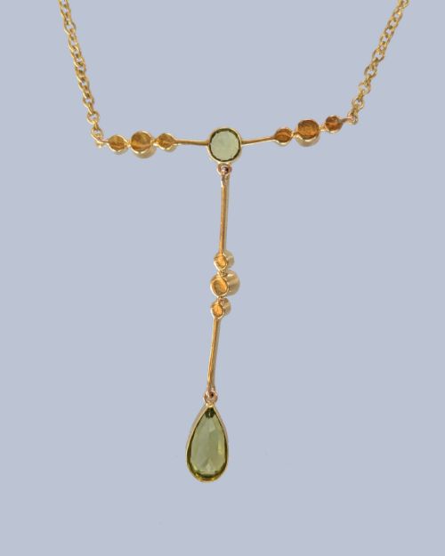 fig 4. An Edwardian 15ct gold lavalier pendant necklace featuring a central round peridot, seed pearl accents, and a suspended pear-cut peridot drop.