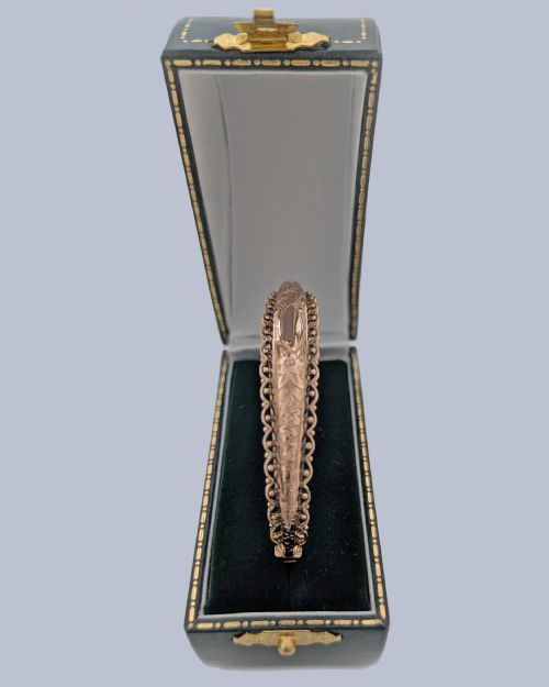 fig 2. An Edwardian 9ct rose gold hinged bangle with foliate engraving, beaded border trim, and a safety chain.