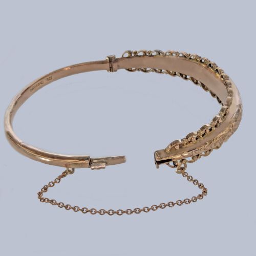 fig 3. An Edwardian 9ct rose gold hinged bangle with foliate engraving, beaded border trim, and a safety chain.