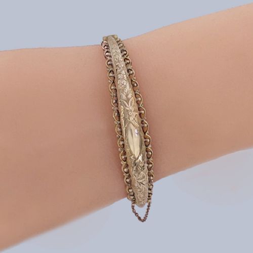 fig 7. An Edwardian 9ct rose gold hinged bangle with foliate engraving, beaded border trim, and a safety chain.