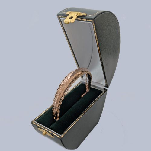 fig 8. An Edwardian 9ct rose gold hinged bangle with foliate engraving, beaded border trim, and a safety chain.