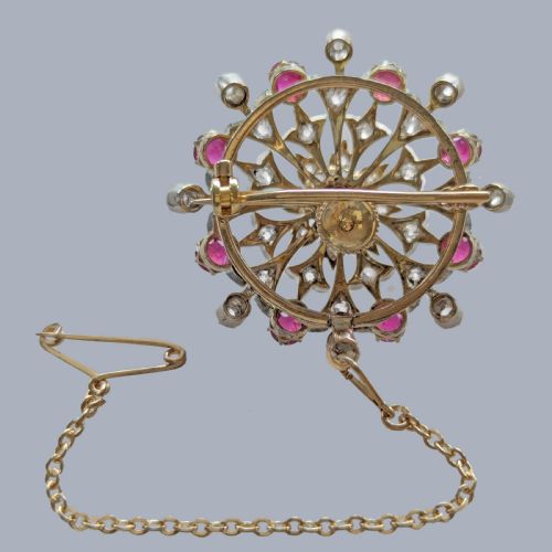 fig 5. A circular Victorian brooch rendered in silver and gold, featuring a central round ruby surrounded by intricate diamond-set starburst openwork and an outer border of alternating rubies and diamonds.