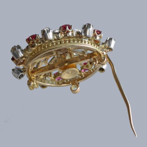 fig 6. A circular Victorian brooch rendered in silver and gold, featuring a central round ruby surrounded by intricate diamond-set starburst openwork and an outer border of alternating rubies and diamonds.