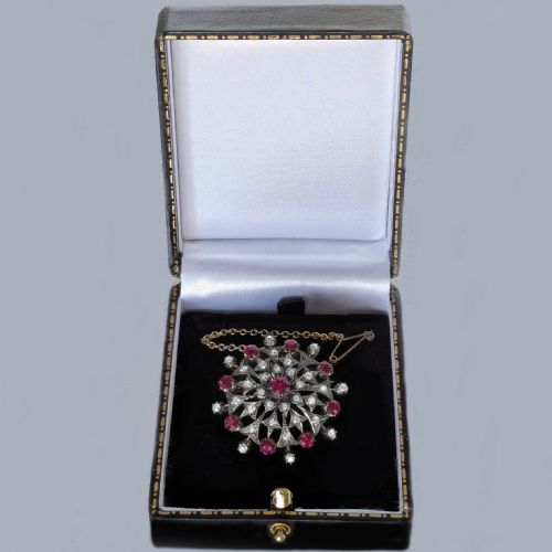 fig 7. A circular Victorian brooch rendered in silver and gold, featuring a central round ruby surrounded by intricate diamond-set starburst openwork and an outer border of alternating rubies and diamonds.