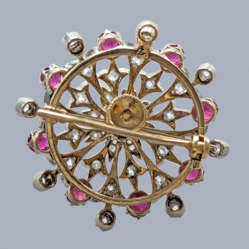 fig 8. A circular Victorian brooch rendered in silver and gold, featuring a central round ruby surrounded by intricate diamond-set starburst openwork and an outer border of alternating rubies and diamonds.