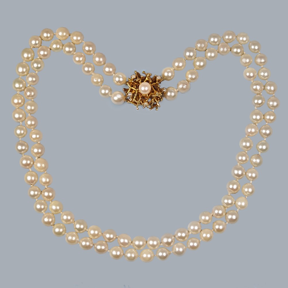 A double strand cream pearl necklace featuring an abstract textured gold centre clasp with a central pearl accent.