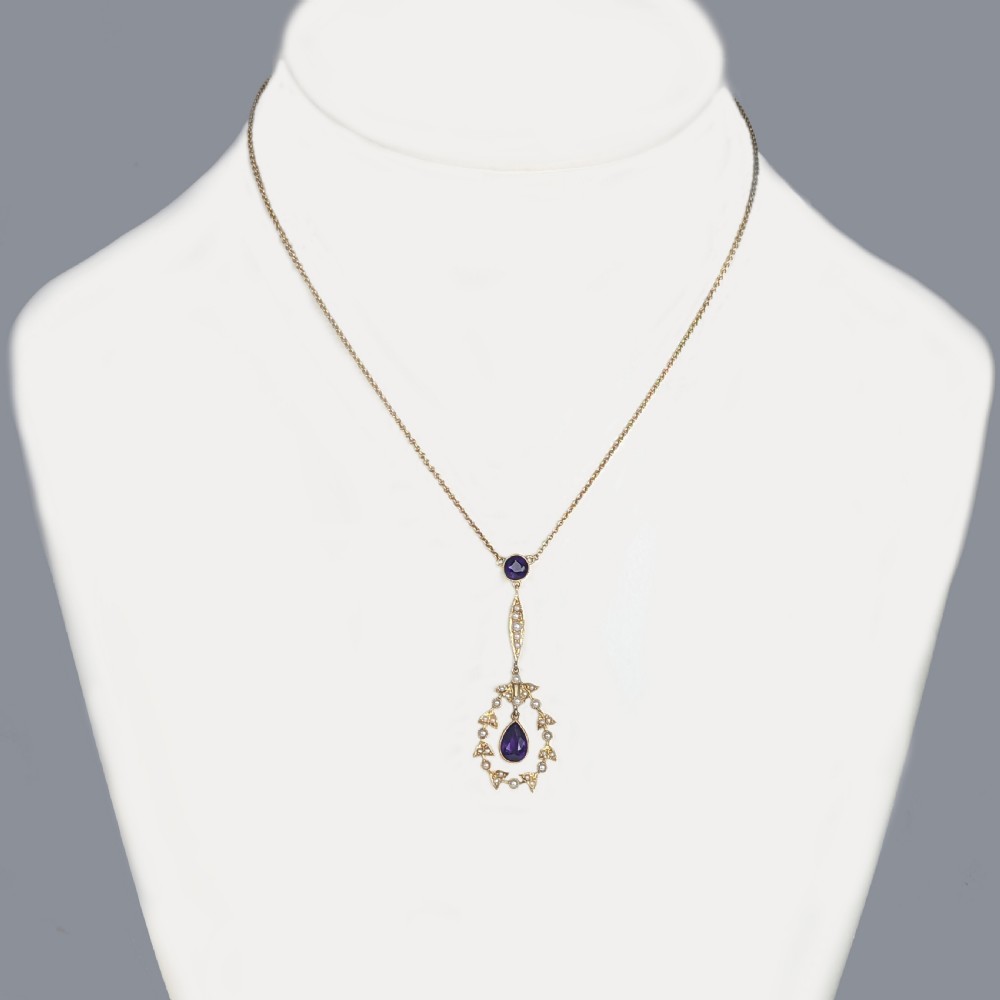 An Edwardian 15ct gold pendant featuring a circular accent set with a seed pearl, suspending a linear bar and pear-cut aquamarine gemstone on a fine gold chain. View II