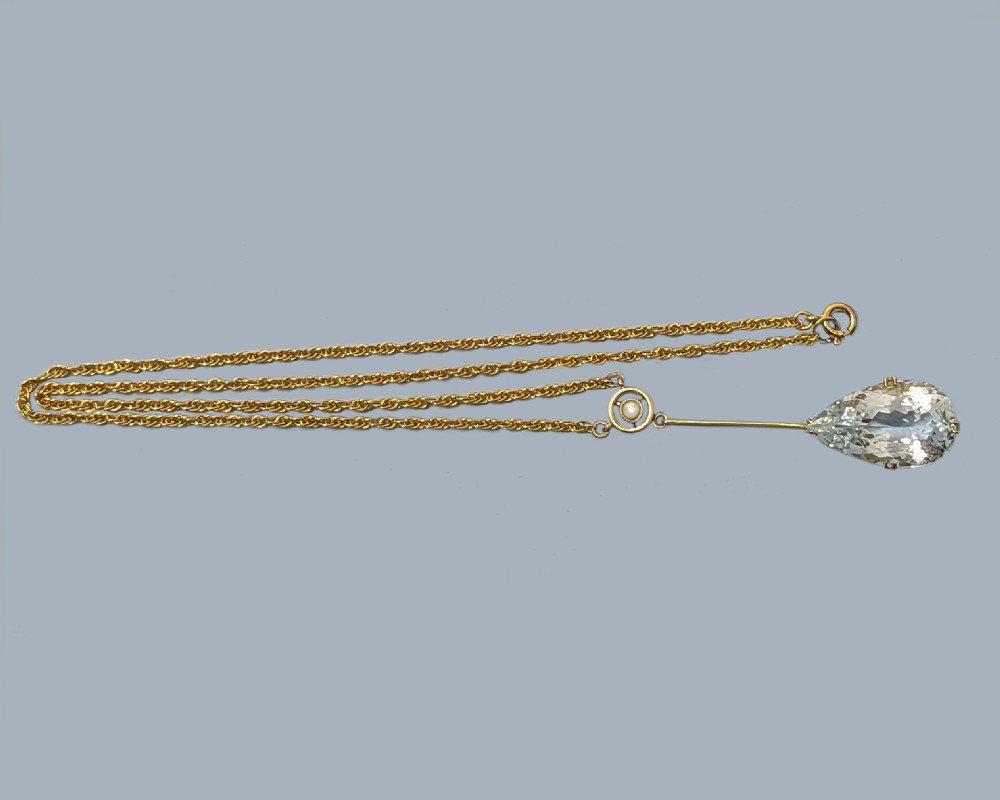 An Edwardian 15ct gold pendant featuring a circular accent set with a seed pearl, suspending a linear bar and pear-cut aquamarine gemstone on a fine gold chain. View III