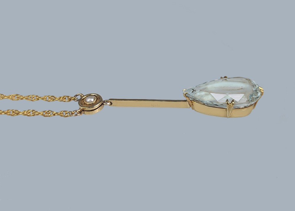 An Edwardian 15ct gold pendant featuring a circular accent set with a seed pearl, suspending a linear bar and pear-cut aquamarine gemstone on a fine gold chain. View IV