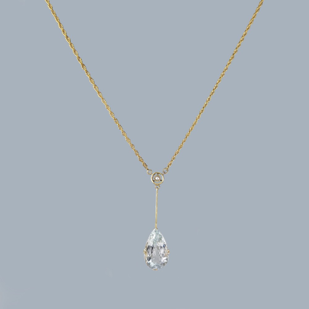 An Edwardian 15ct gold pendant featuring a circular accent set with a seed pearl, suspending a linear bar and pear-cut aquamarine gemstone on a fine gold chain. View VI
