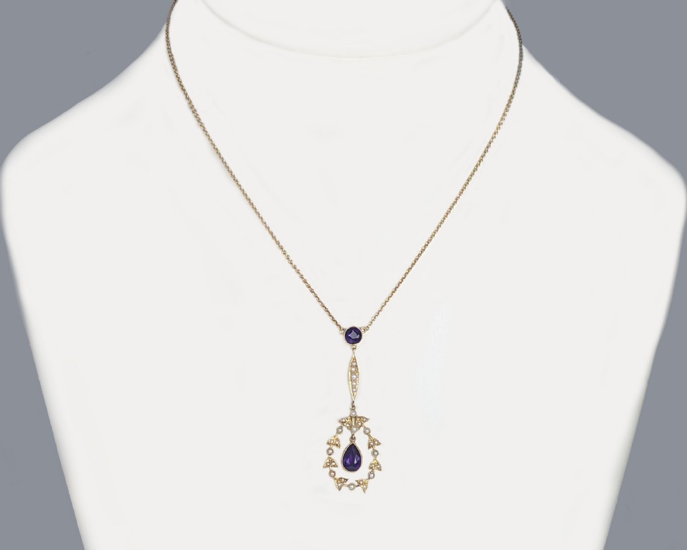 An Edwardian 15ct gold pendant featuring a circular accent set with a seed pearl, suspending a linear bar and pear-cut aquamarine gemstone on a fine gold chain. View VIII