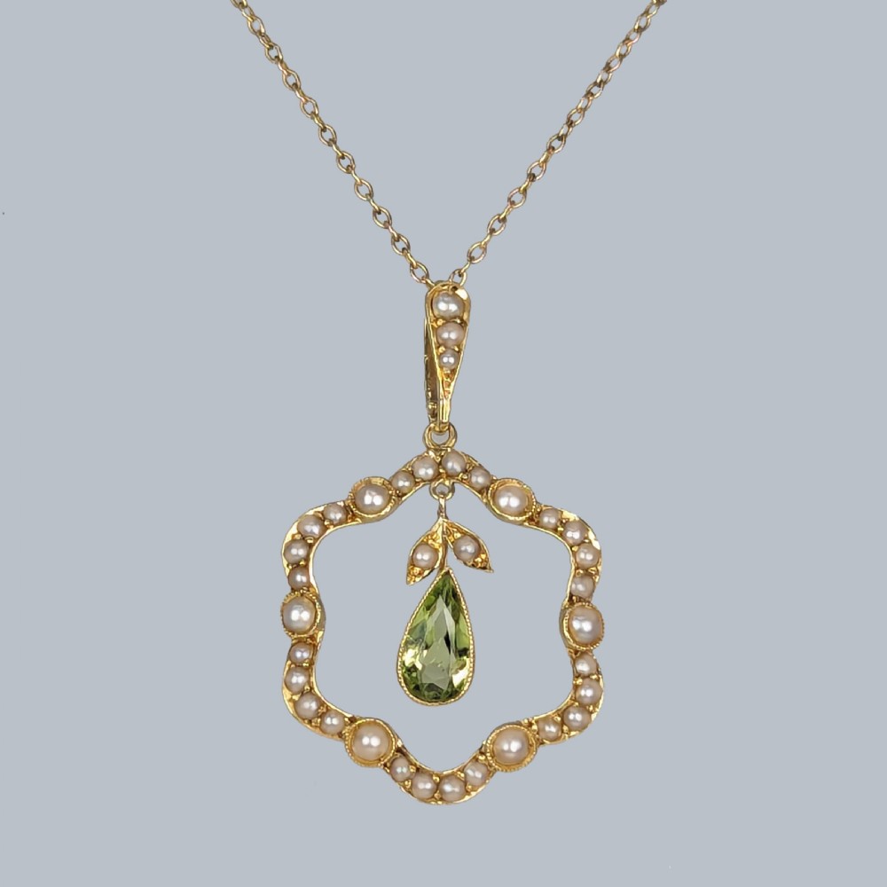 An Art Nouveau 15ct gold openwork pendant set with seed pearls around the rim and suspending a central pear-shaped peridot gemstone.