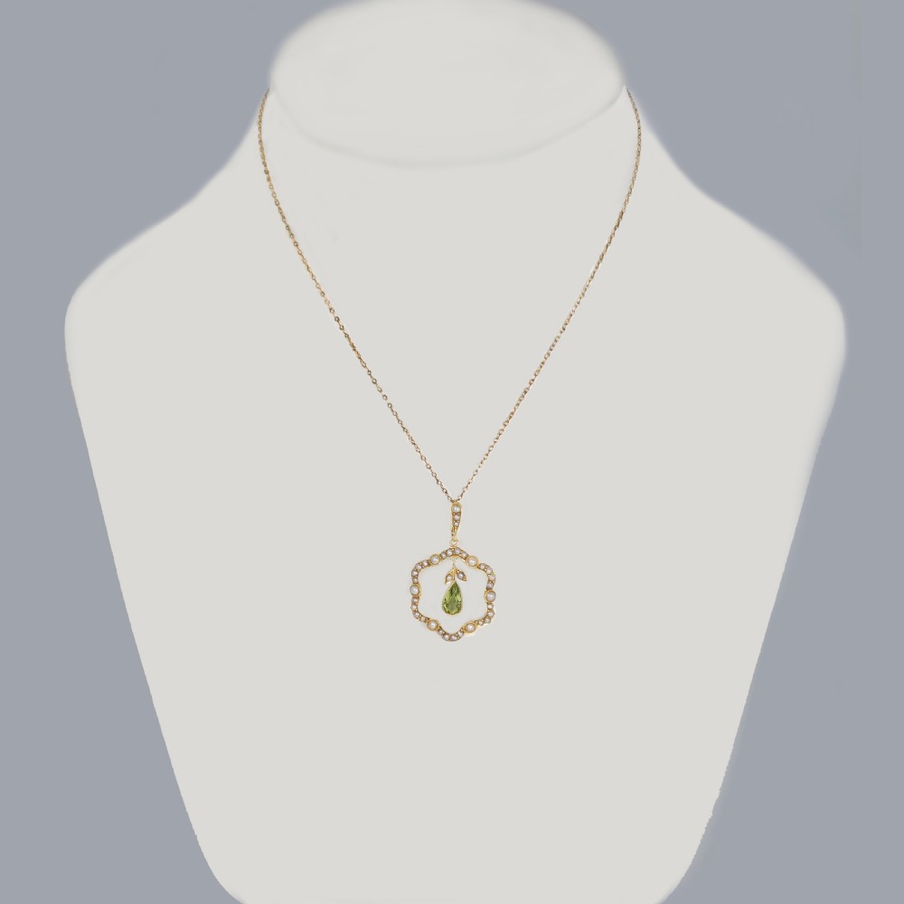 An Art Nouveau 15ct gold openwork pendant set with seed pearls around the rim and suspending a central pear-shaped peridot gemstone. View II