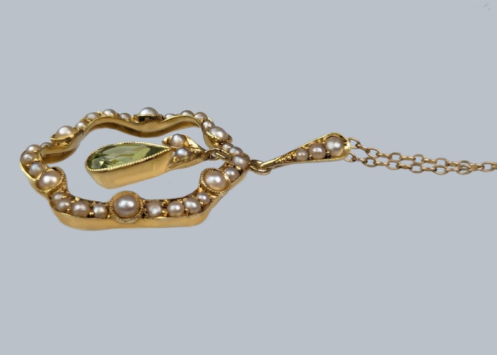An Art Nouveau 15ct gold openwork pendant set with seed pearls around the rim and suspending a central pear-shaped peridot gemstone. View V