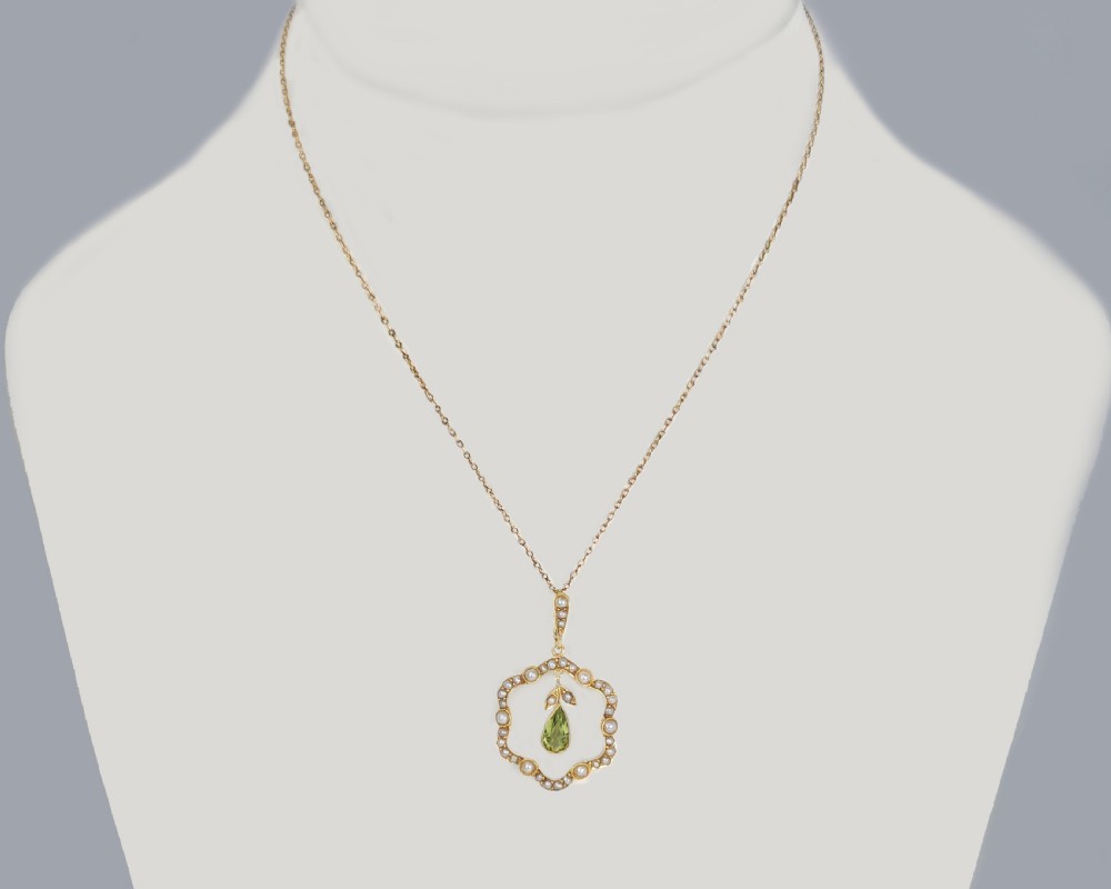 An Art Nouveau 15ct gold openwork pendant set with seed pearls around the rim and suspending a central pear-shaped peridot gemstone. View VIII