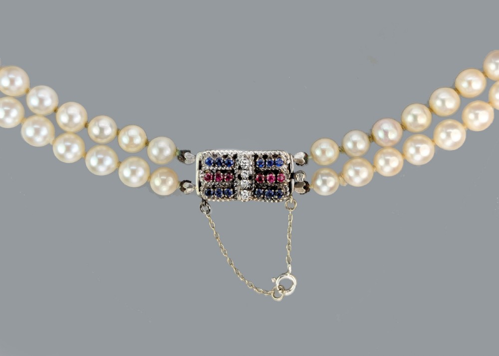 A double strand cream cultured pearl necklace featuring a rectangular 18ct gold clasp set with sapphires, rubies, and diamonds. View V