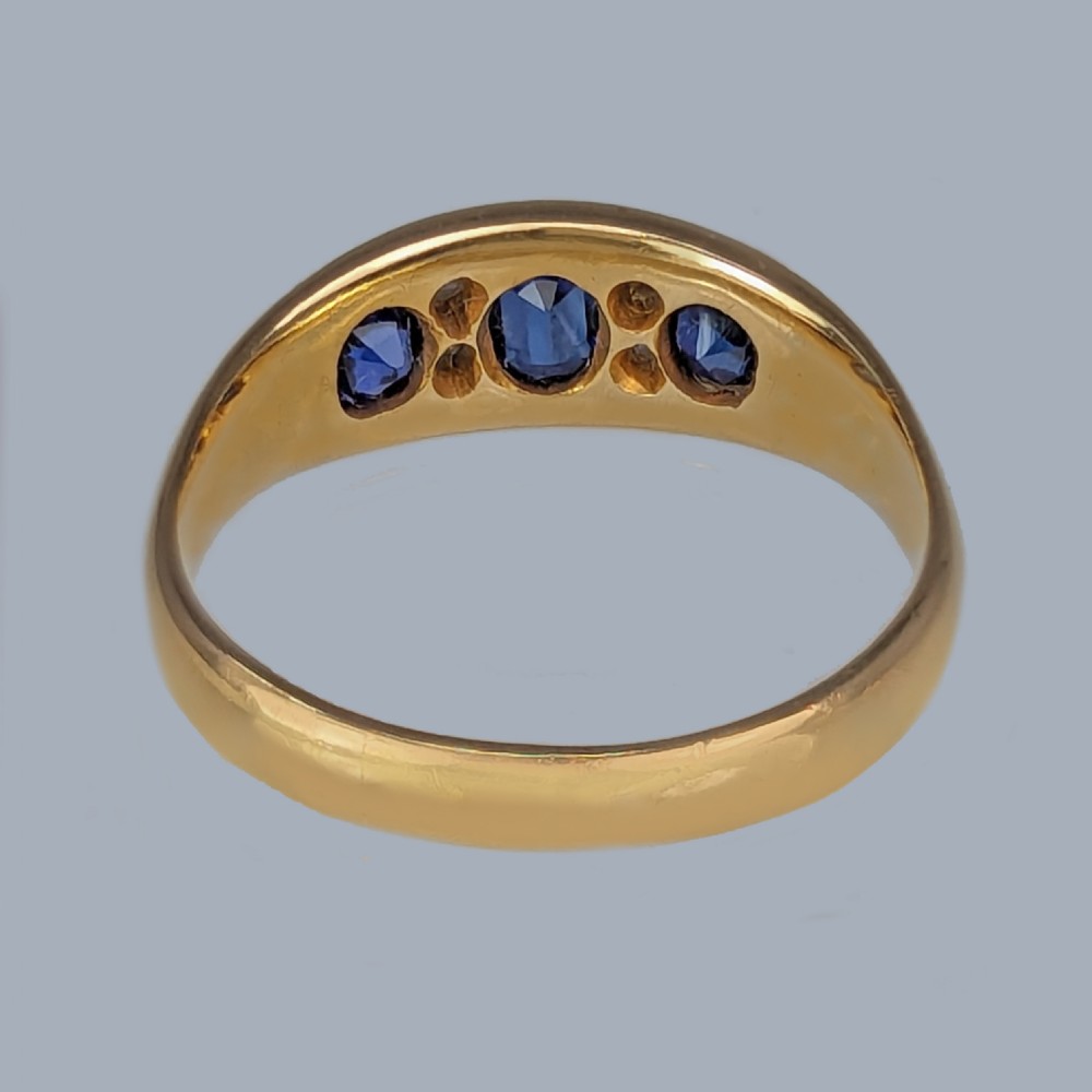 An antique Victorian 18ct yellow gold ring set with three blue sapphires and four old-cut diamonds in a boat-shaped setting with carved shoulders. View VII
