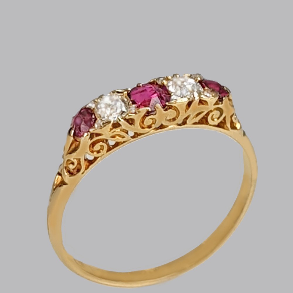 An 18ct yellow gold Victorian five-stone ring featuring alternating red rubies and old-cut diamonds set in a carved scrollwork gallery.