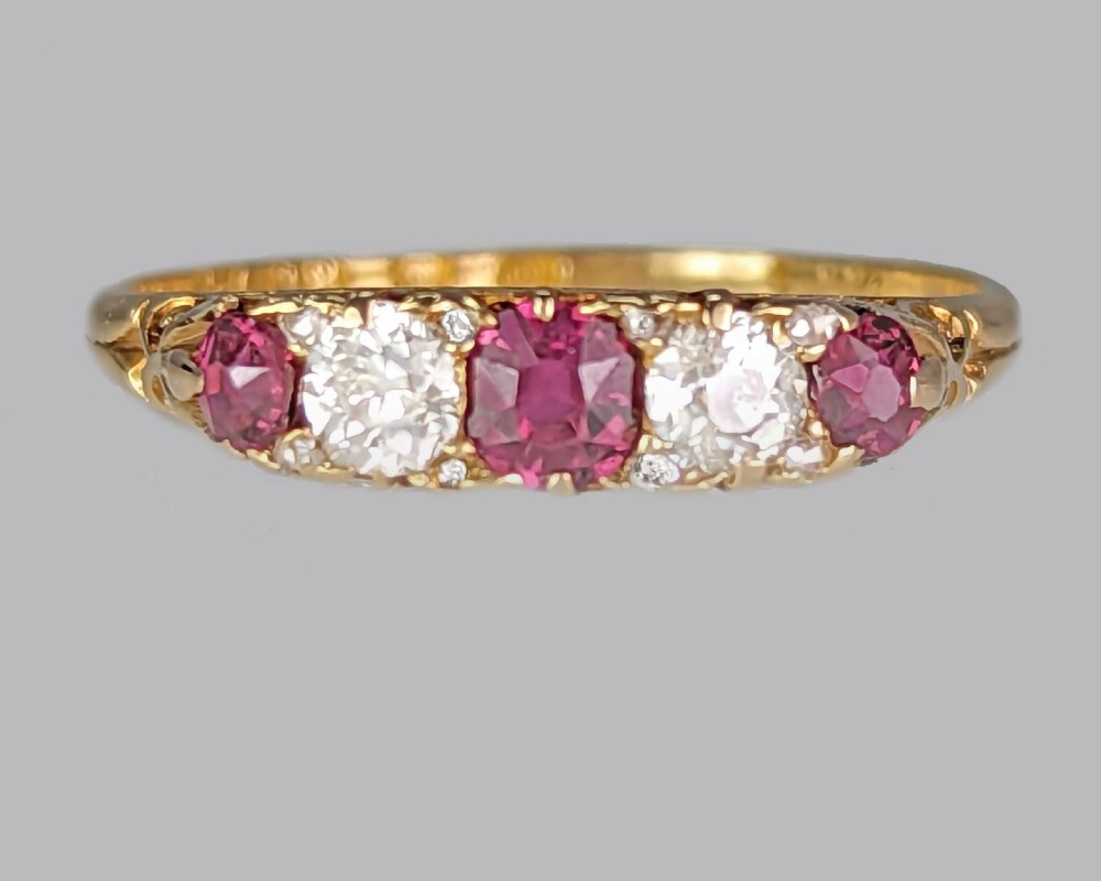 An 18ct yellow gold Victorian five-stone ring featuring alternating red rubies and old-cut diamonds set in a carved scrollwork gallery. View II