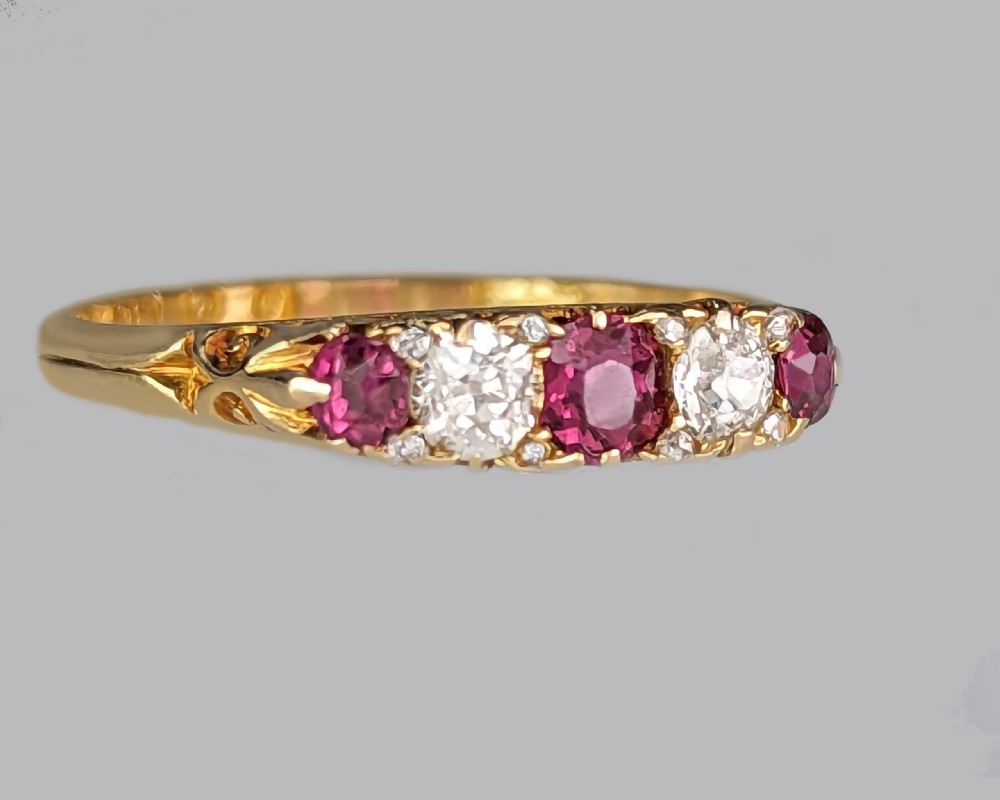 An 18ct yellow gold Victorian five-stone ring featuring alternating red rubies and old-cut diamonds set in a carved scrollwork gallery. View VII