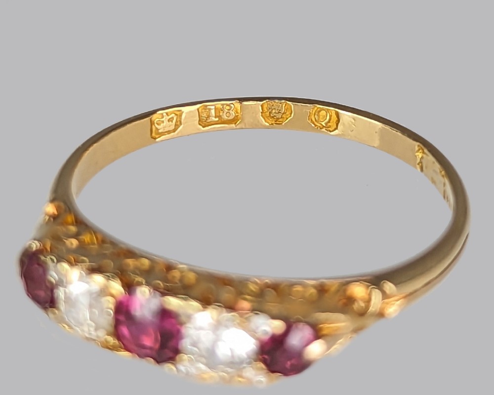 An 18ct yellow gold Victorian five-stone ring featuring alternating red rubies and old-cut diamonds set in a carved scrollwork gallery. View VIII