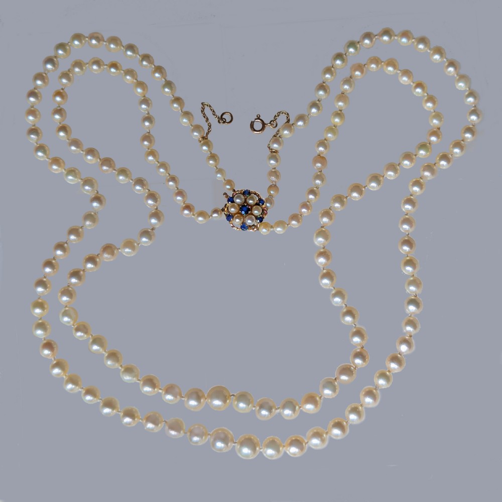A double strand vintage pearl necklace featuring cream pearls and a circular floral 9ct gold clasp set with pearls and blue sapphires.
