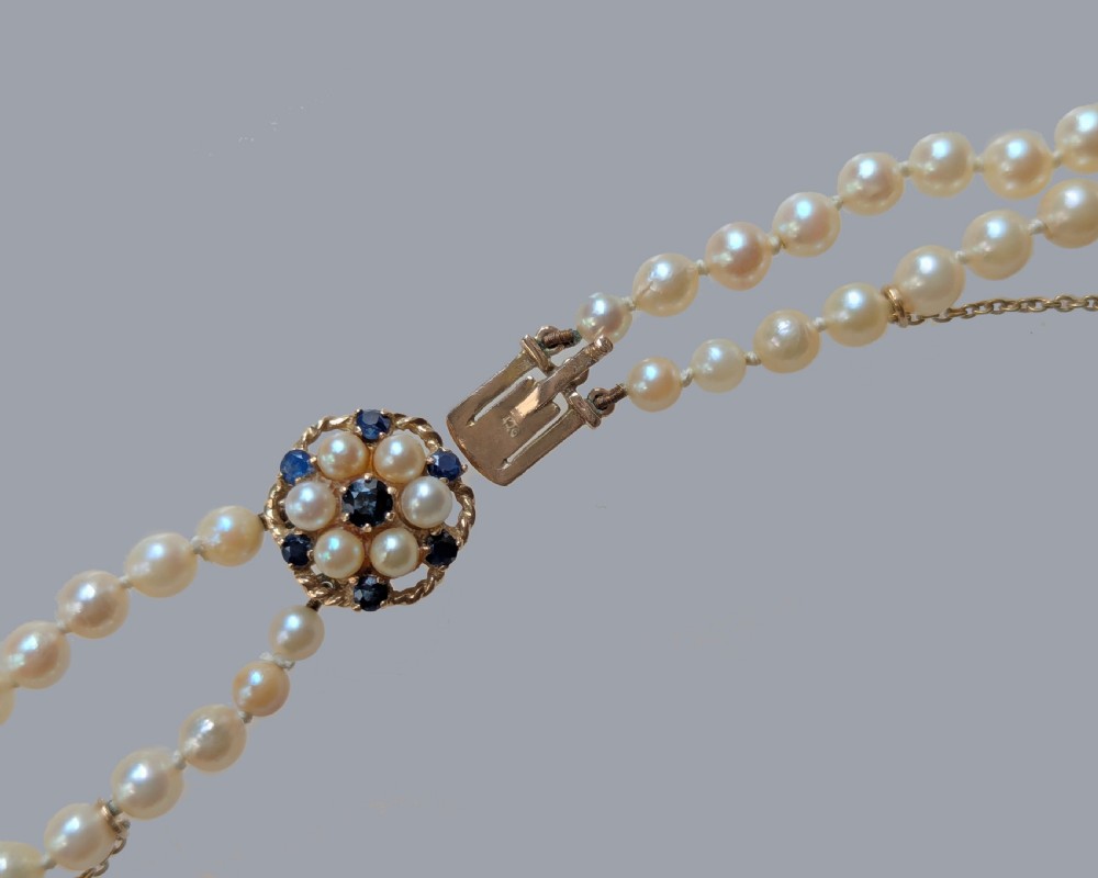 A double strand vintage pearl necklace featuring cream pearls and a circular floral 9ct gold clasp set with pearls and blue sapphires. View IV