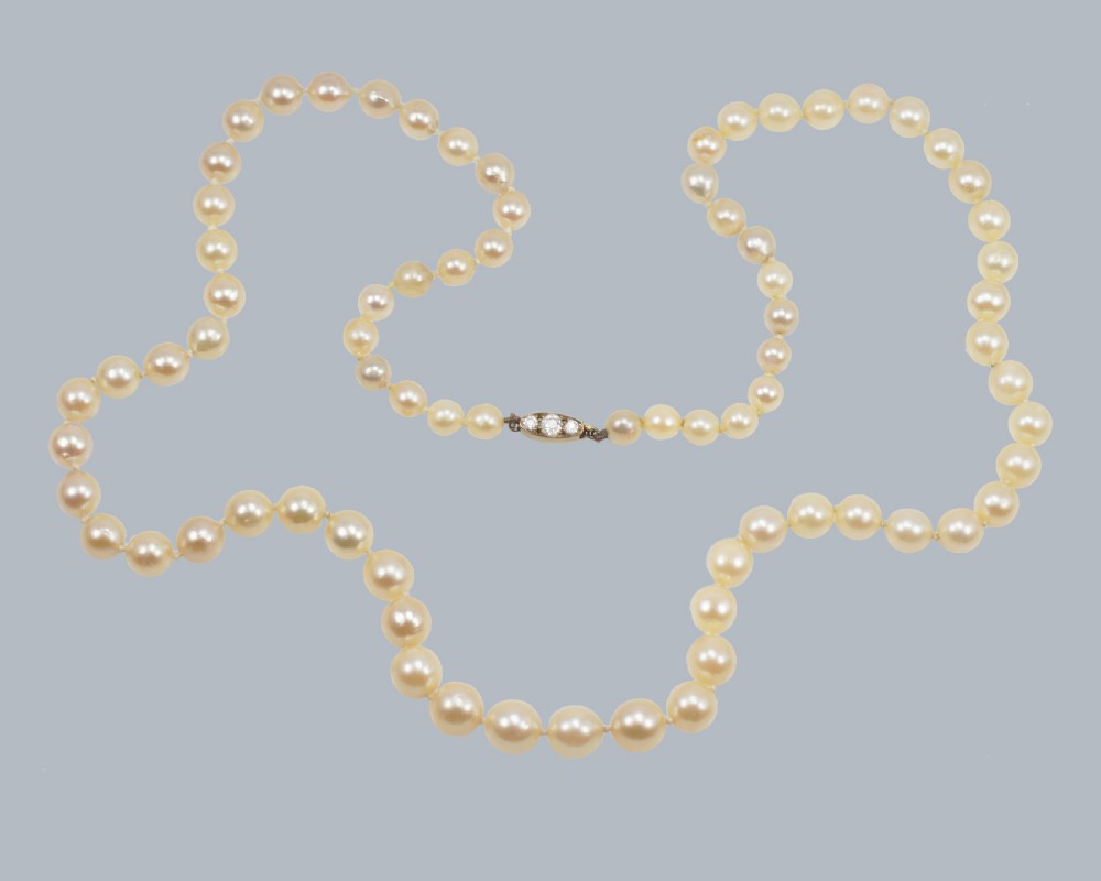 A single strand of cream-coloured pearls fitted with a central clasp set with three old cut diamonds.