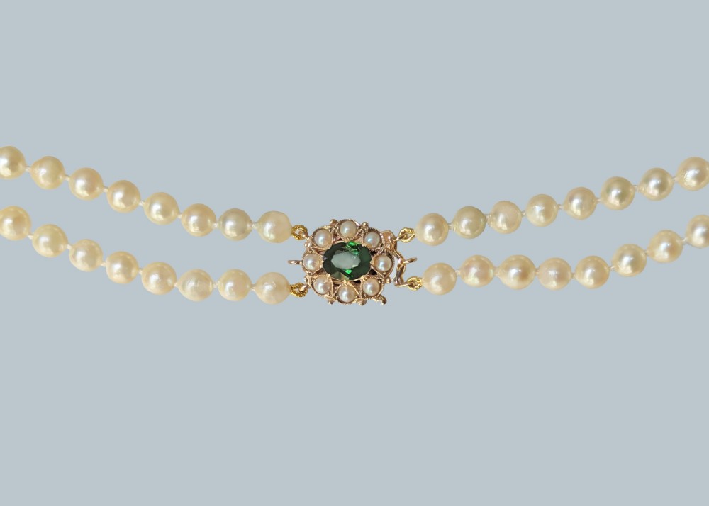 A double strand cream pearl necklace featuring an ornate gold clasp set with a central round green tourmaline stone. View III