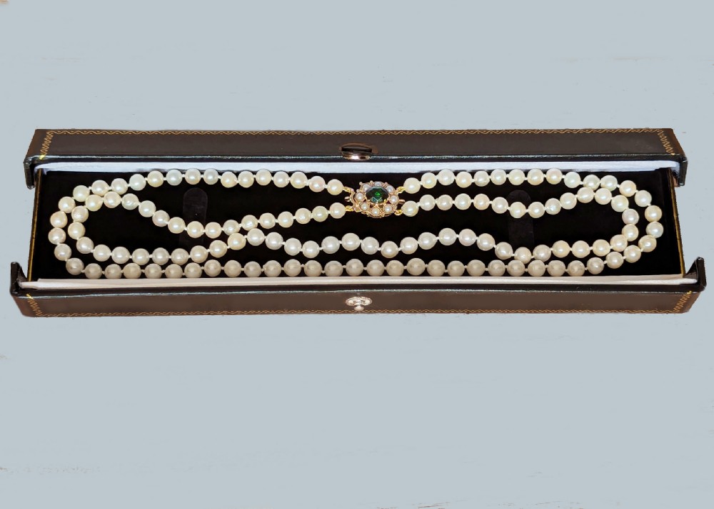 A double strand cream pearl necklace featuring an ornate gold clasp set with a central round green tourmaline stone. View V