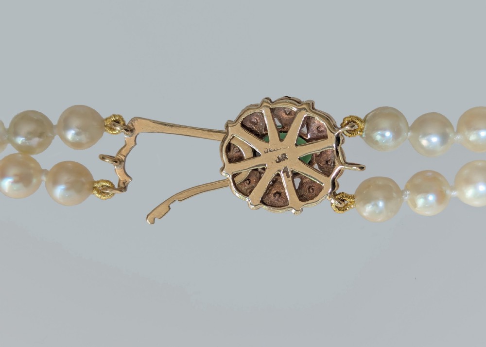A double strand cream pearl necklace featuring an ornate gold clasp set with a central round green tourmaline stone. View VII