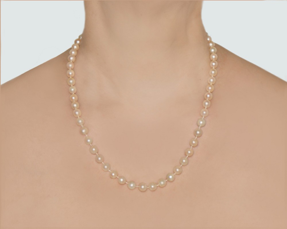 A single strand of uniform cream pearls worn around a neck, secured with a fine metal clasp.