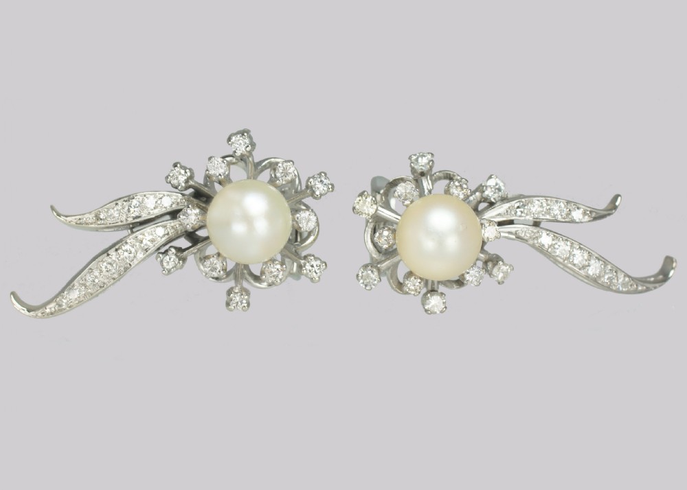 A pair of 1950s 18ct white gold clip-on earrings featuring central cultured pearls surrounded by diamond-set floral sprays and sweeping curved accents. View VII