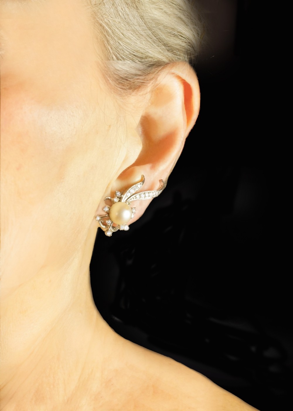 A pair of 1950s 18ct white gold clip-on earrings featuring central cultured pearls surrounded by diamond-set floral sprays and sweeping curved accents. View X